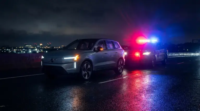Modern electric SUV on a dark highway surrounded by flashing emergency lights.